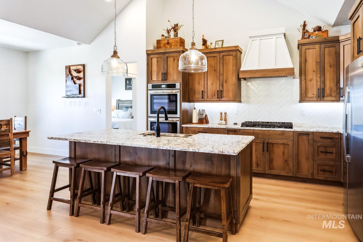 18658 Tranquil Place Caldwell, ID 83607 - Photo 10 of 44 Kitchen featuring a large island with granite-style countertop, natural wood cabinetry, stainless steel double ovens, a built-in cooktop, and a white herringbone-patterned tile backsplash