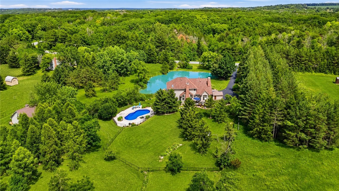 2057 Stirnie Road Victor, NY 14564 - Photo 45 of 48 Another aerial perspective highlights the layout of this 5.10 acre country estate. An expansive paved driveway stretches from the road, winding past pristine lawns and mature pine trees down to the main residence and the massive detached barn structure, demonstrating the impressive scope and seclusion of the estate.