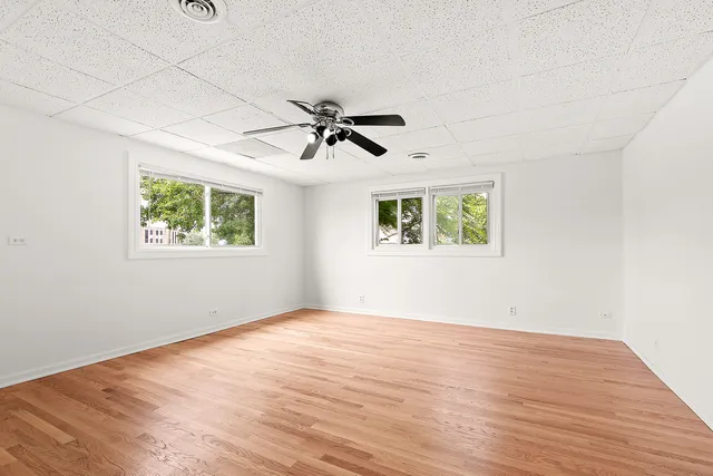 an empty room with wooden floor ceiling fan and windows