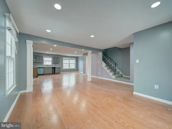 a view of empty room with wooden floor and kitchen