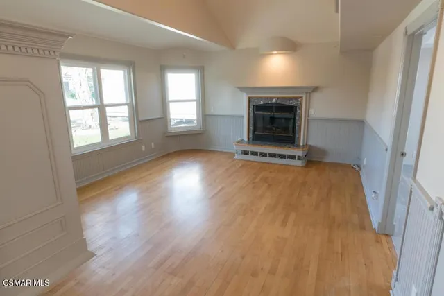 an empty room with wooden floor fireplace and windows