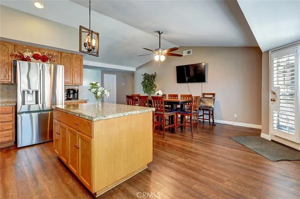 a kitchen with stainless steel appliances granite countertop a refrigerator a stove top oven a dining table and chairs with wooden floor