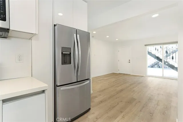 a view of a refrigerator in kitchen and an empty room with wooden floor
