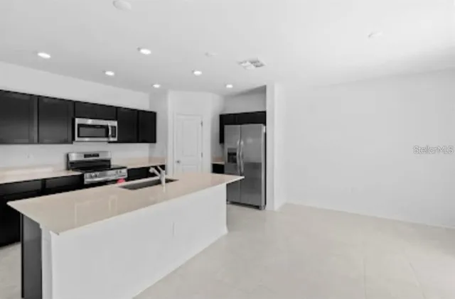 a large white kitchen with stainless steel appliances a sink dishwasher a refrigerator and a stove with wooden floor