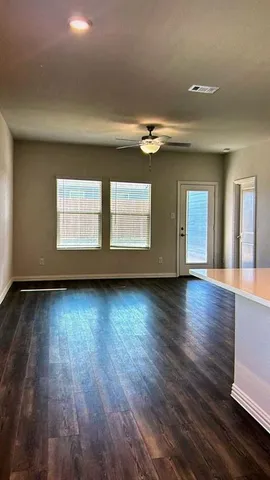 an empty room with wooden floor fan and windows
