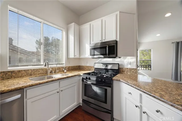 a kitchen with granite countertop a sink stainless steel appliances and white cabinets
