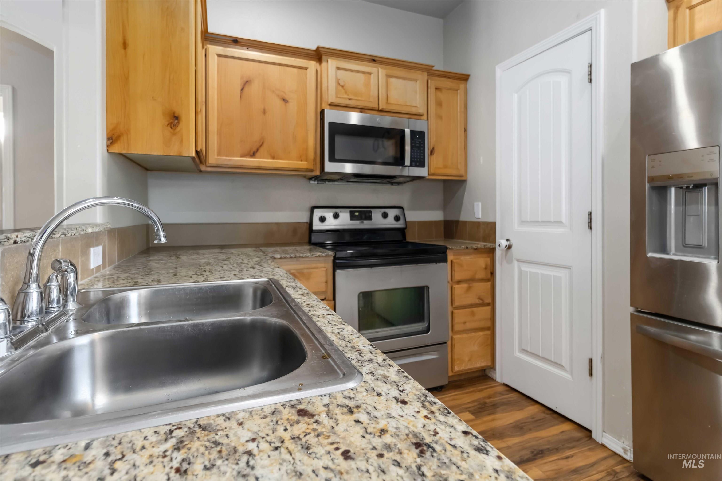 16053 Sunnyfield Avenue Caldwell, ID 83607 - Photo 11 of 35 Kitchen with stainless steel appliances, dark wood-style flooring, light wood finish cabinets, and light stone countertops