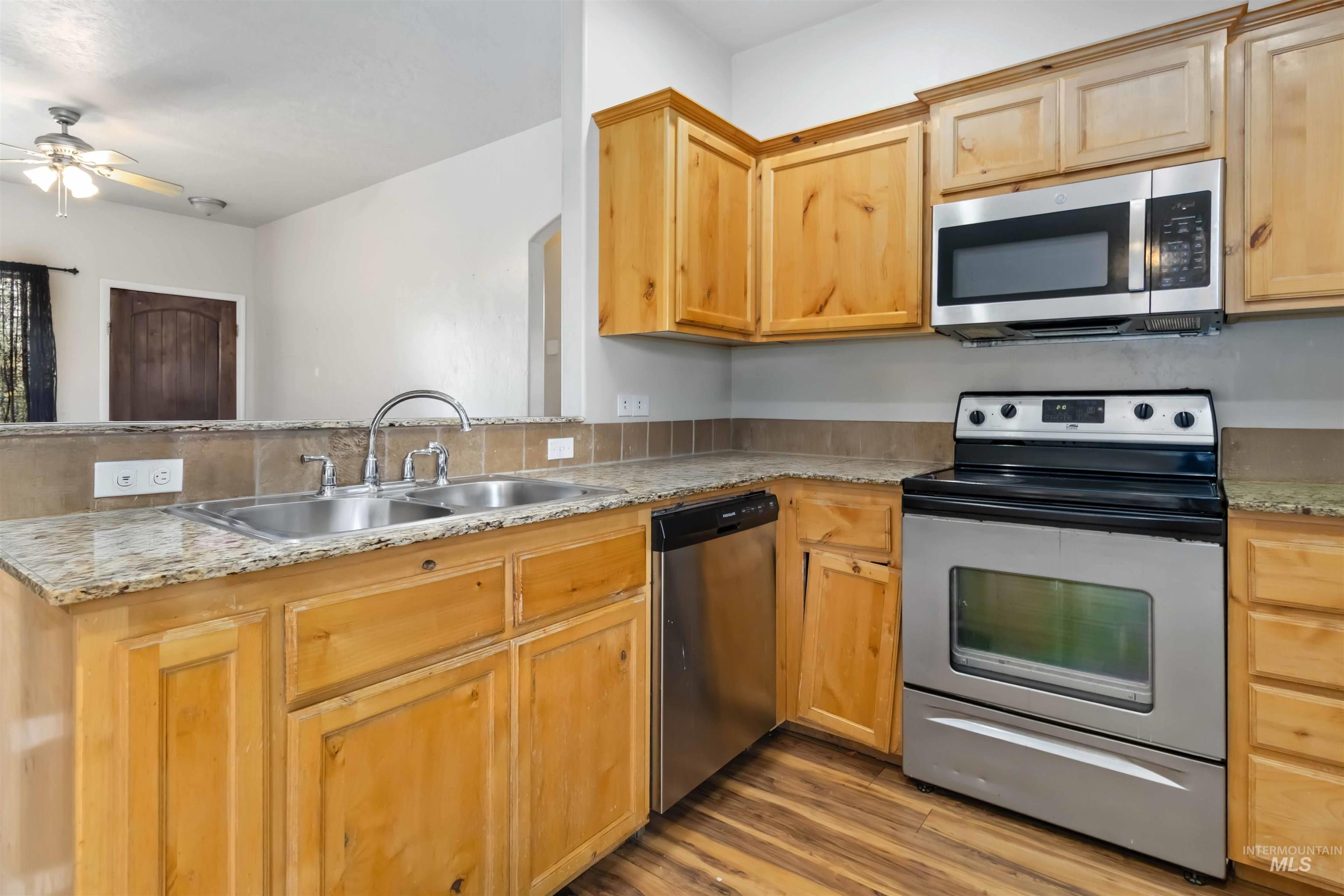 16053 Sunnyfield Avenue Caldwell, ID 83607 - Photo 12 of 35 Kitchen with stainless steel appliances, ceiling fan, light wood finished floors, light stone countertops, and light wood finish cabinetry