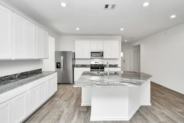 a large kitchen with stainless steel appliances granite countertop a stove a sink a refrigerator and white cabinets with wooden floor