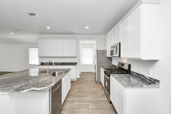 a large kitchen with stainless steel appliances granite countertop a stove top oven a sink a refrigerator and white cabinets