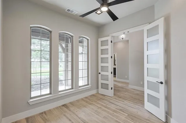 an empty room with wooden floor fan and windows