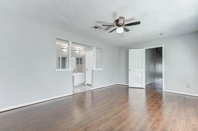 a view of an empty room with wooden floor and a ceiling fan