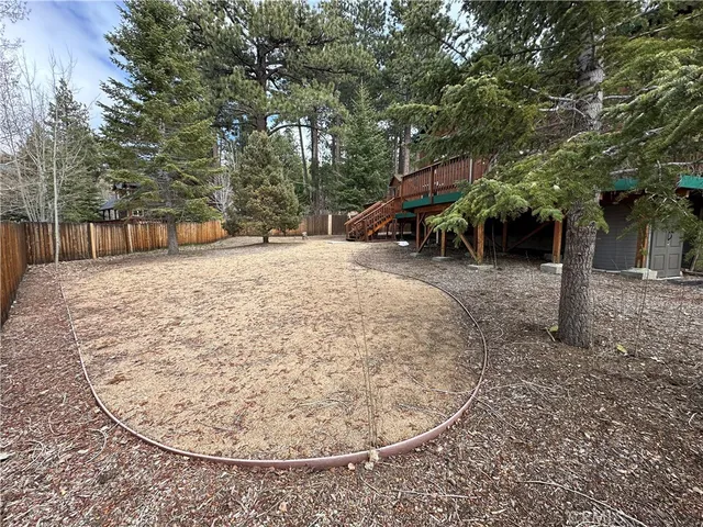 a view of a backyard with large trees and wooden fence
