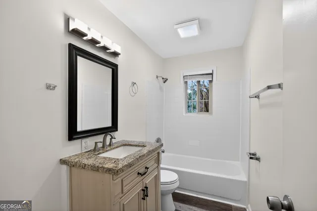 a bathroom with a granite countertop sink a toilet a mirror and shower
