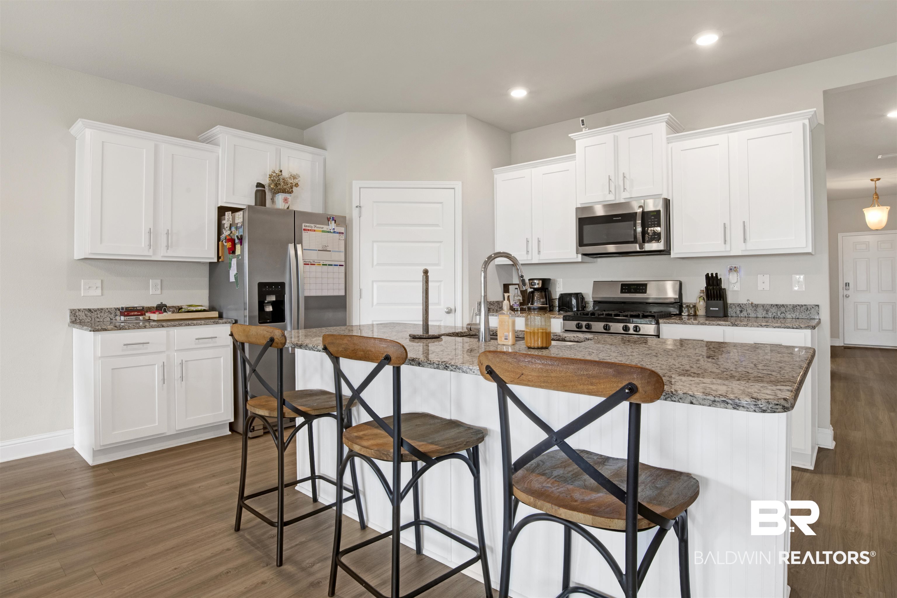 9306 Swan Point Road Daphne, AL 36526 - Photo 9 of 28 Modern kitchen featuring an island with stone countertop, stainless steel appliances, white cabinetry, and wood-finish flooring