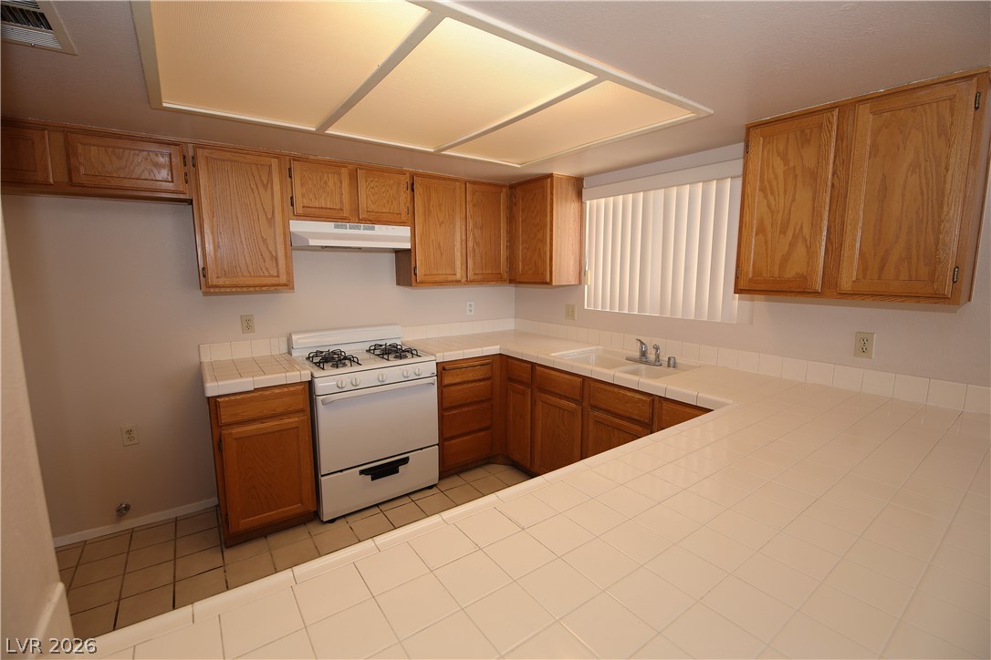 8220 Maplestar Road Las Vegas, NV 89128 - Photo 9 of 29 A functional kitchen features wood cabinetry and ample tiled counter space.