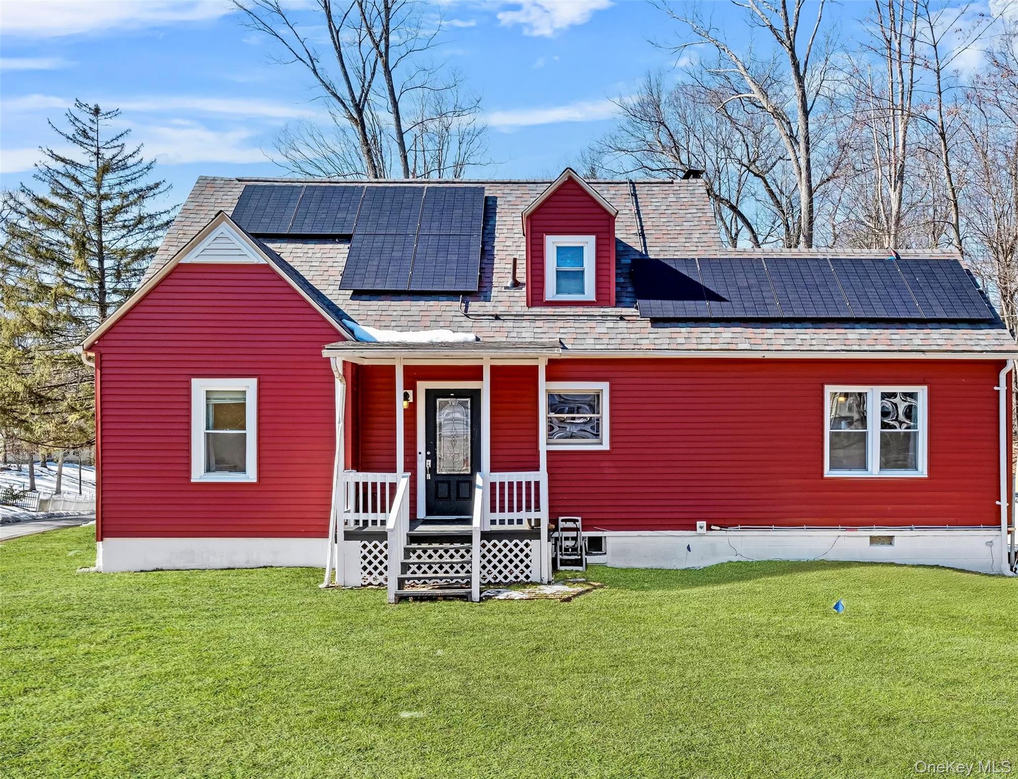 View of front of house with a front lawn, solar panels, and roof with shingles