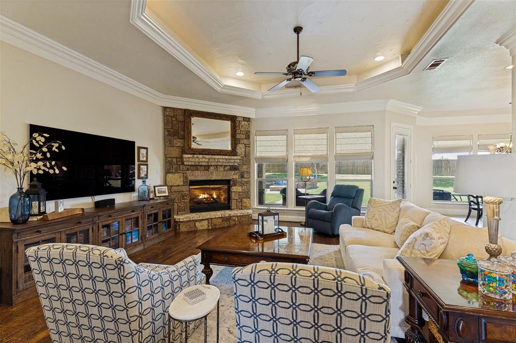 229 Arbor Lane Haslet, TX 76052 - Photo 7 of 34 Spacious living area featuring a stone-clad fireplace, wood-finish flooring, and a tray ceiling with crown molding
