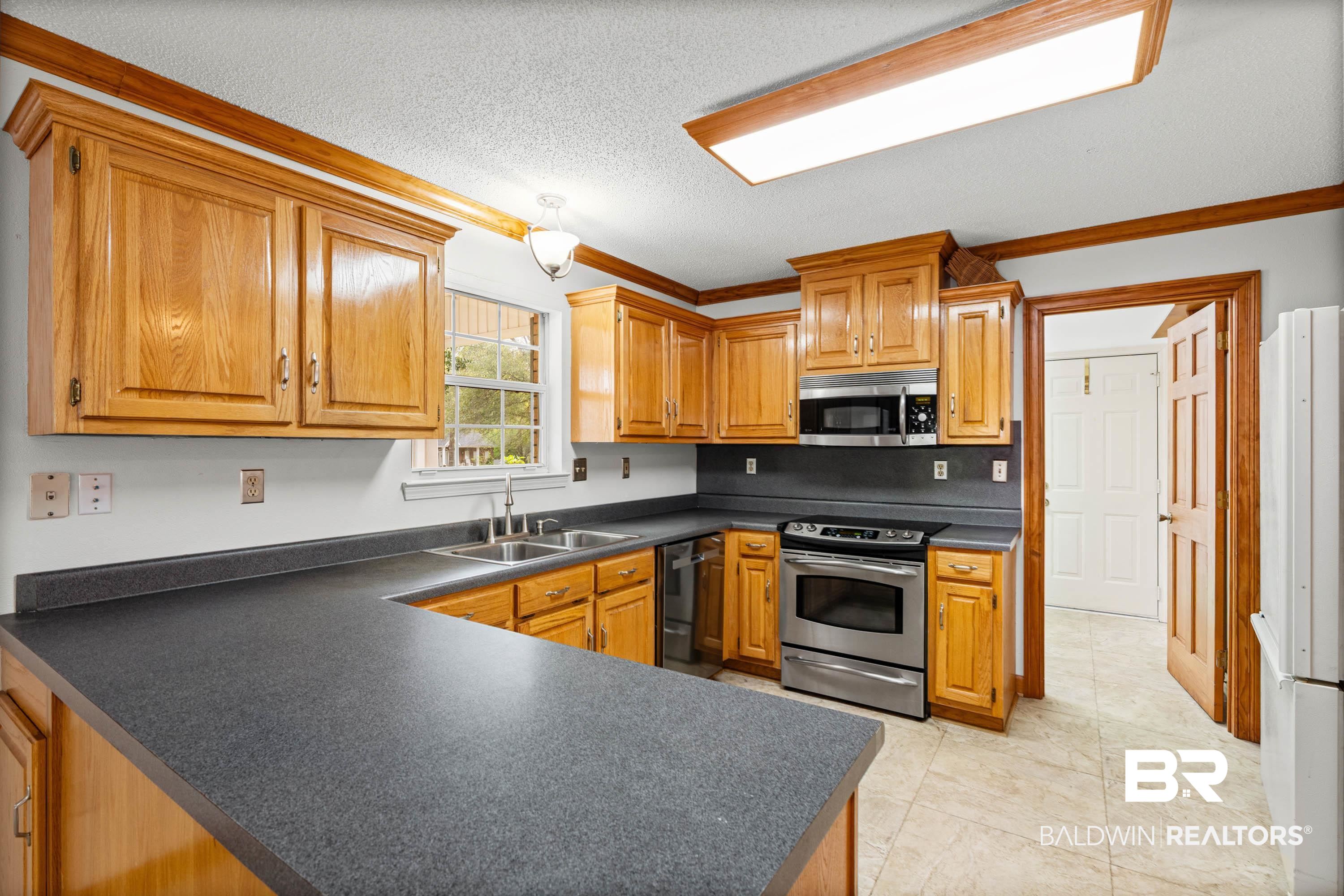 10140 Lakeview Road Bay Minette, AL 36507 - Photo 11 of 35 Kitchen with dark countertops, crown molding, a textured ceiling, wood finish cabinetry, and stainless steel appliances
