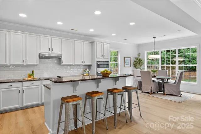 a kitchen with stainless steel appliances granite countertop a stove top oven a sink dishwasher and white cabinets with wooden floor