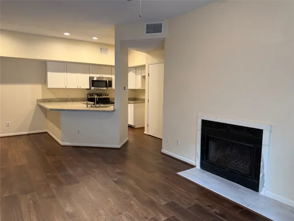 a living room with stainless steel appliances furniture a fireplace and a kitchen view