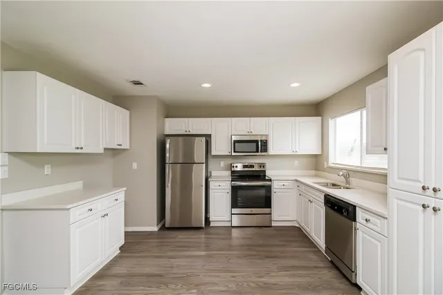 a kitchen with stainless steel appliances granite countertop a stove top oven a sink a refrigerator and white cabinets