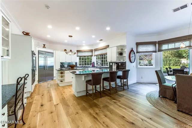 a open kitchen with stainless steel appliances granite countertop a refrigerator a stove top oven a dining table and chairs with wooden floor