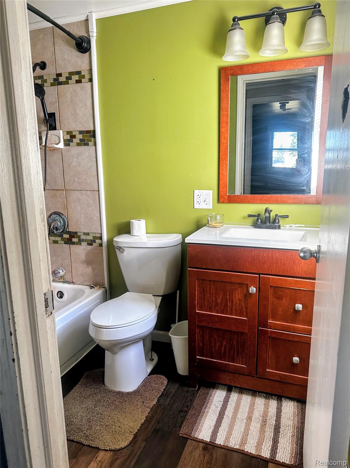 7305 West Gary Road Chesaning, MI 48616 - Photo 17 of 27 Bathroom featuring a vanity with a white countertop and wood-finish cabinetry, a mirror with an orange frame, a three-light fixture, and a tiled shower-bath combination