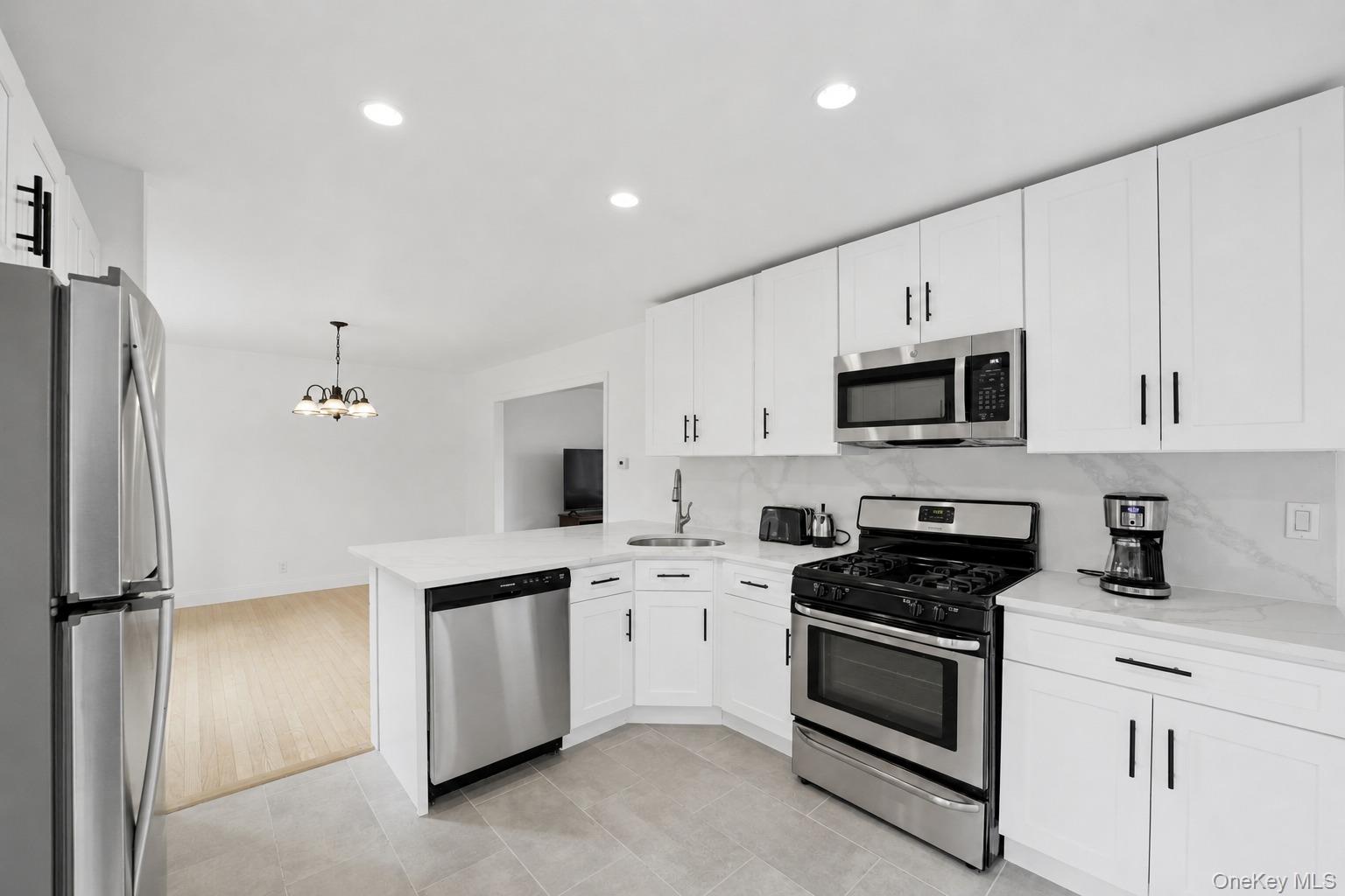 144 Bell Road Scarsdale, NY 10583 - Photo 13 of 49 Modern kitchen featuring white cabinetry with black hardware, stainless steel appliances, a white countertop, and a tile backsplash