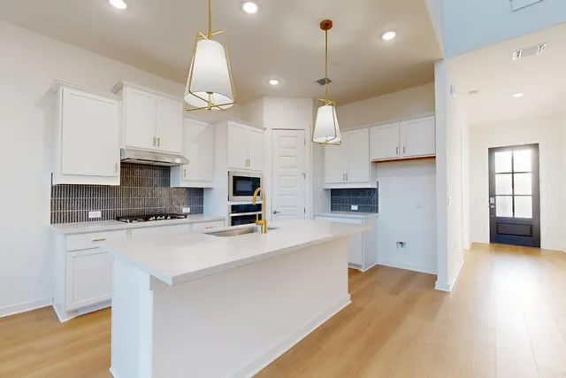 a kitchen with stainless steel appliances a stove a sink dishwasher a refrigerator white cabinets and wooden floor