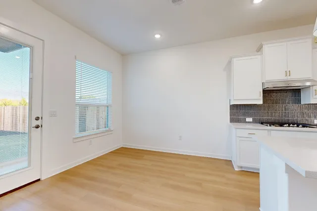 a view of empty room with wooden floor and kitchen