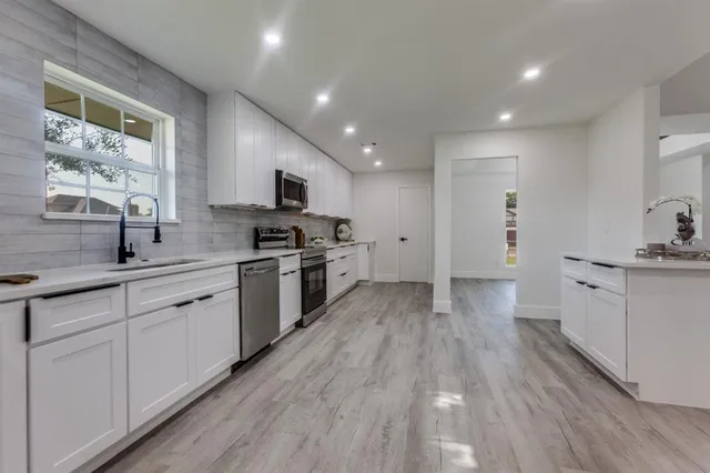 a kitchen with white cabinets a sink a window and stainless steel appliances