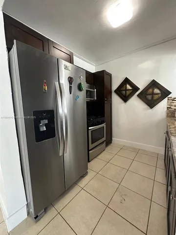 a view of a refrigerator in kitchen and an empty room with wooden floor
