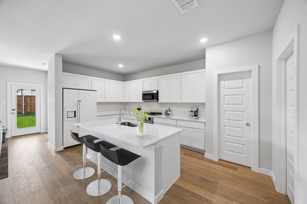 1448 Companero Street Haslet, TX 76052 - Photo 6 of 35 a kitchen with a refrigerator a stove and white cabinets with wooden floor