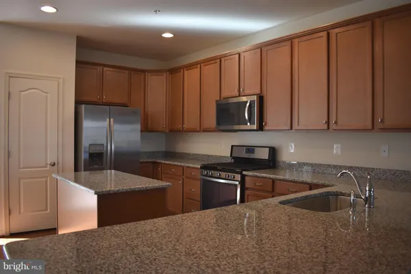 a kitchen with stainless steel appliances granite countertop a sink a stove and a refrigerator with wooden cabinets