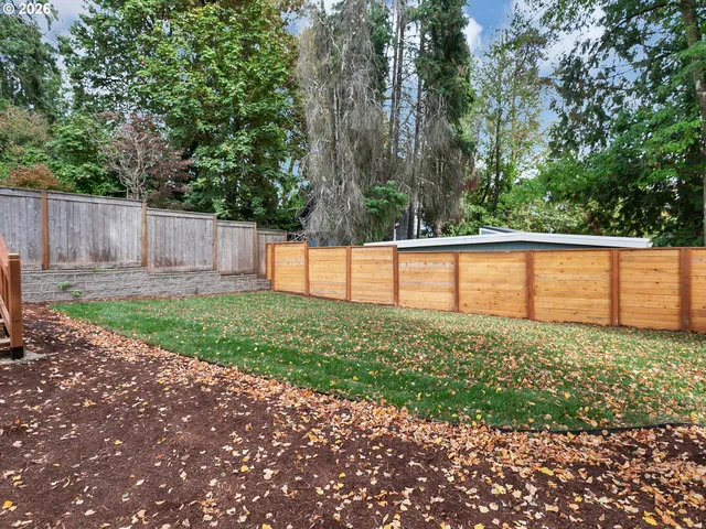 a view of a backyard with large trees and wooden fence