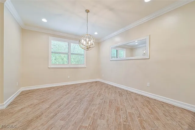 an empty room with wooden floor chandelier and windows