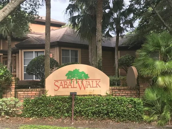 a sign that is sitting in front of a brick house with a small yard