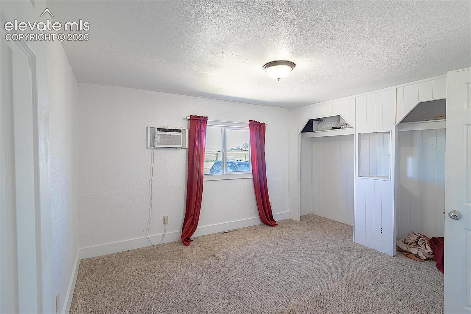 3425 Wiesner Road Calhan, CO 80808 - Photo 11 of 25 Unfurnished bedroom featuring a wall mounted AC, light colored carpet, a textured ceiling, a closet, and baseboards