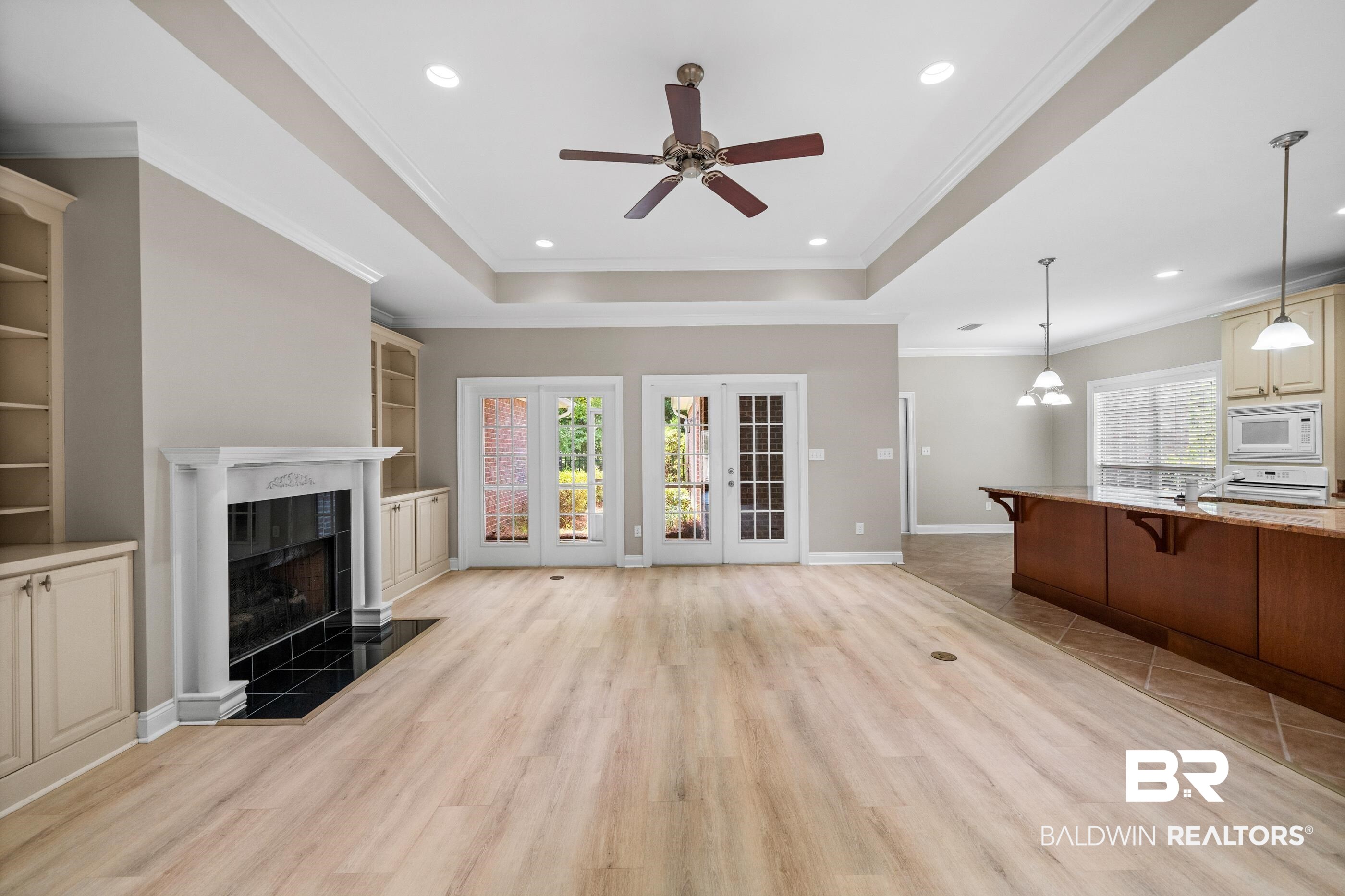 303 Savannah Circle Foley, AL 36535 - Photo 8 of 34 Spacious living area featuring wood-finish flooring, a tray ceiling with recessed lighting and a ceiling fan, a fireplace with a white mantel and black tile surround, built-in cabinetry, and French doors