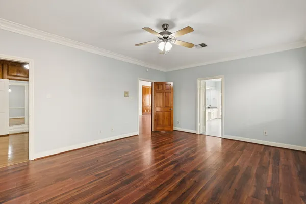 a view of an empty room with wooden floor and a ceiling fan