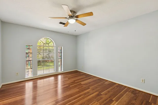 an empty room with wooden floor fan and windows