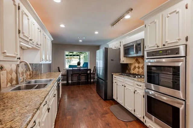 a kitchen with stainless steel appliances granite countertop a stove top oven a sink dishwasher and white cabinets with wooden floor