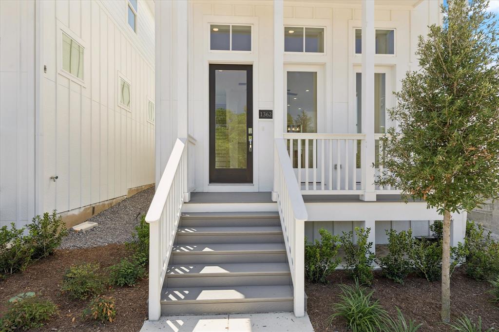 1362 East Crosby Road Carrollton, TX 75006 - Photo 6 of 22 Inviting front entry featuring a dark-framed glass door, white board and batten siding, a covered porch with white railings, and a mature tree