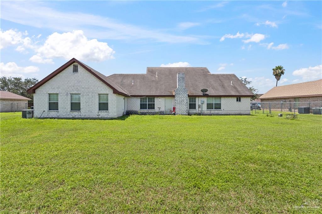 402 Mockingbird Lane Edcouch, TX 78538 - Photo 20 of 25 Expansive rear lawn featuring a white brick exterior with a multi-level roofline, a prominent chimney, multiple windows, and a partially fenced perimeter