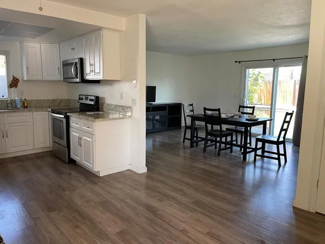 a kitchen with stainless steel appliances granite countertop wooden floors a stove top oven a dining table and chairs