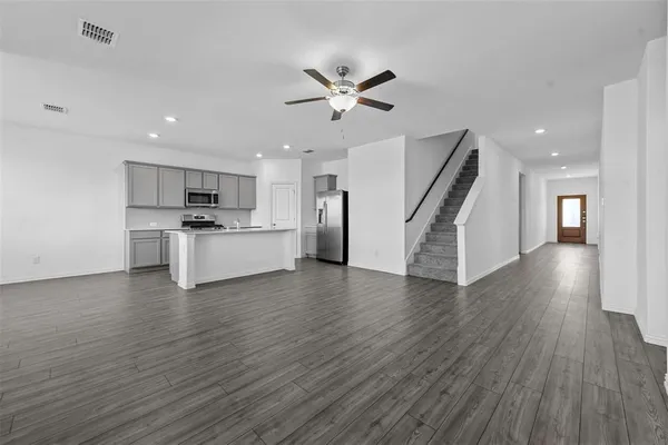 a view of an empty room with wooden floor a ceiling fan and windows