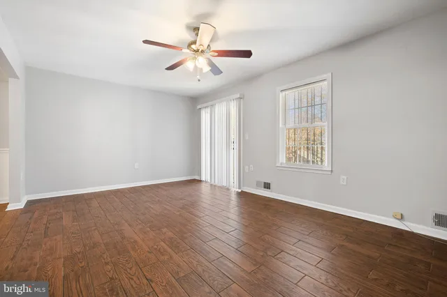 an empty room with wooden floor chandelier fan and windows