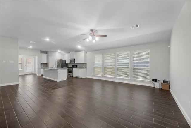 a view of an empty room with wooden floor and a kitchen