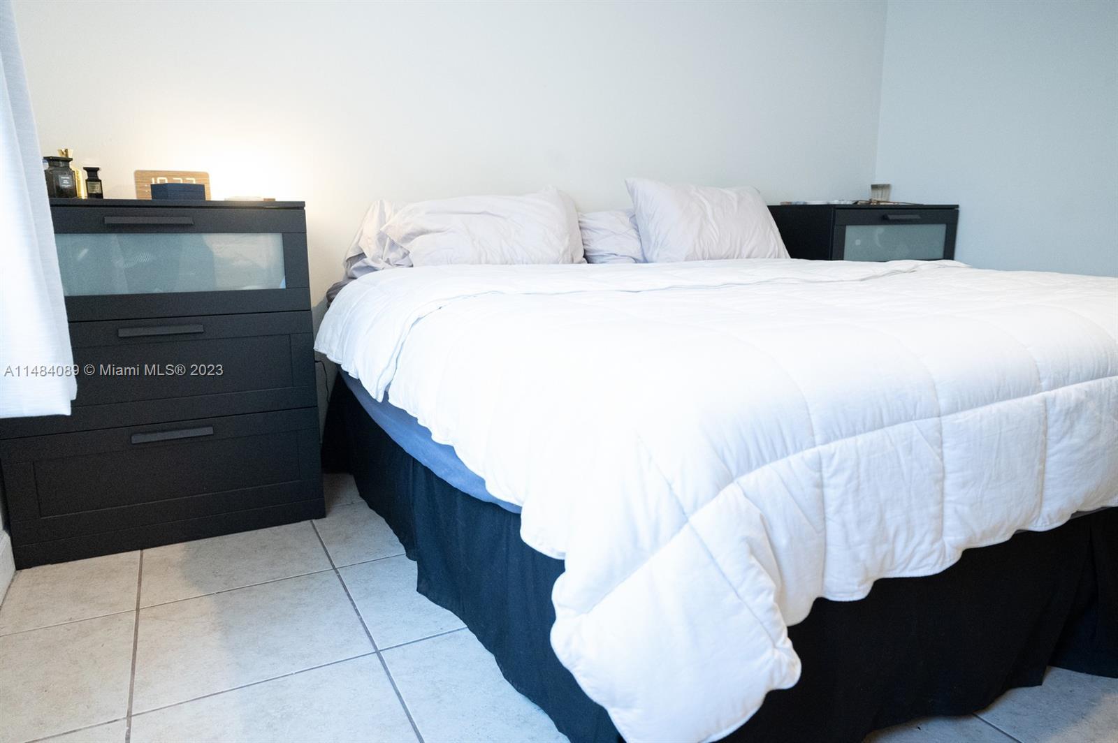 7715 Southwest 86th Street, Unit A2307 Miami, FL 33143 - Photo 52 of 89 a spacious bedroom with a bed and a lamp on dresser